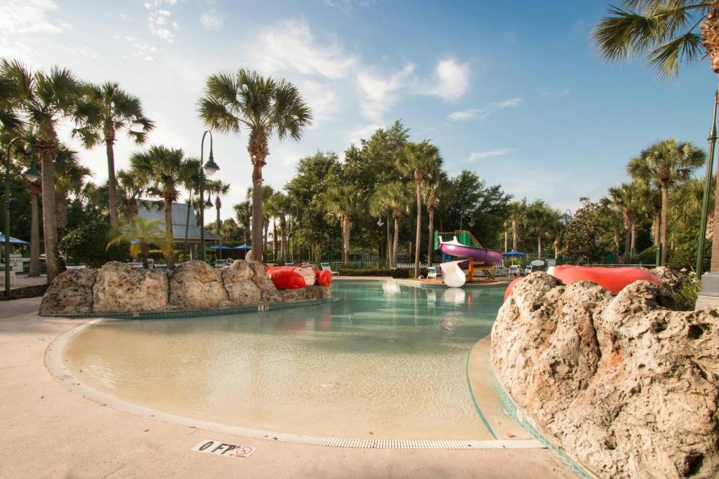 piscina que imita praia com uma rampa de acesso e tobogã mais ao fundo e palmeiras ao redor no SpringHill Suites by Marriott Orlando Lake Buena Vista South, um dos hotéis em Kissimmee