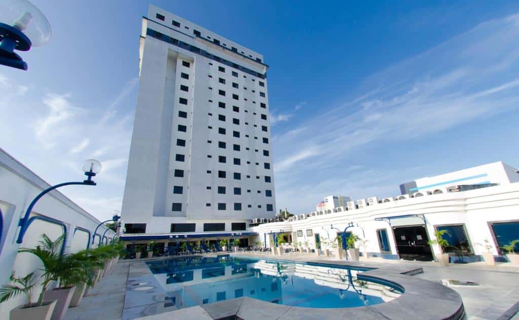 Prédio alto com uma grande piscina em frente. Dos lados é possível ver paredes, plantas e uma entrada para o hotel. Foto para ilustrar post de hotéis em Belém do Pará.