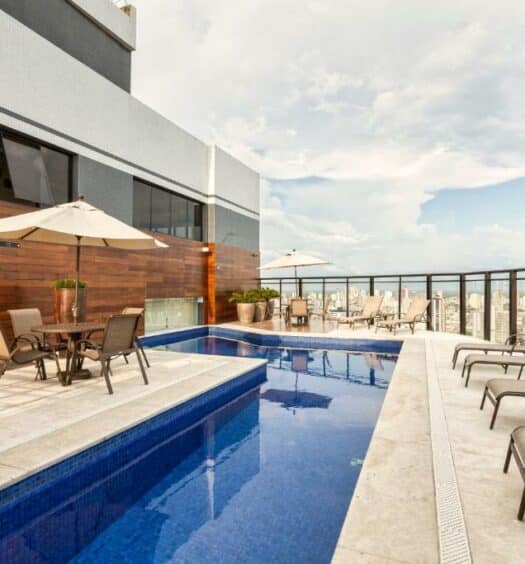 Piscina a céu aberto em uma varanda. Cadeiras de piscina e mesinhas com guarda-sol estão em volta. Imagem para ilustrar post de hotéis em Belém do Pará.