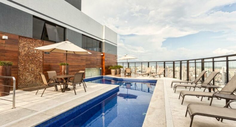 Piscina a céu aberto em uma varanda. Cadeiras de piscina e mesinhas com guarda-sol estão em volta. Imagem para ilustrar post de hotéis em Belém do Pará.