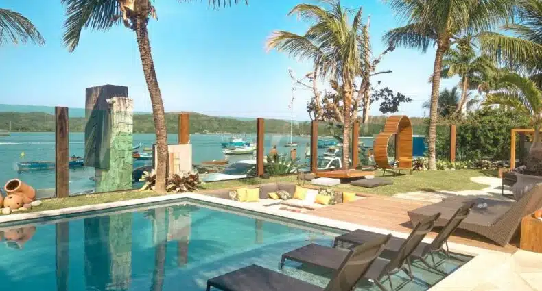 Piscina com cadeiras para tomar sol em frente ao mar com barcos. Imagem para ilustrar o post hotéis para Cabo Frio.
