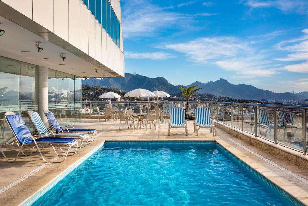Uma piscina com cadeiras ao redor. Vista da piscina para a cidade. Foto para ilustrar post sobre hotéis perto do Consulado Americano no Rio de Janeiro.