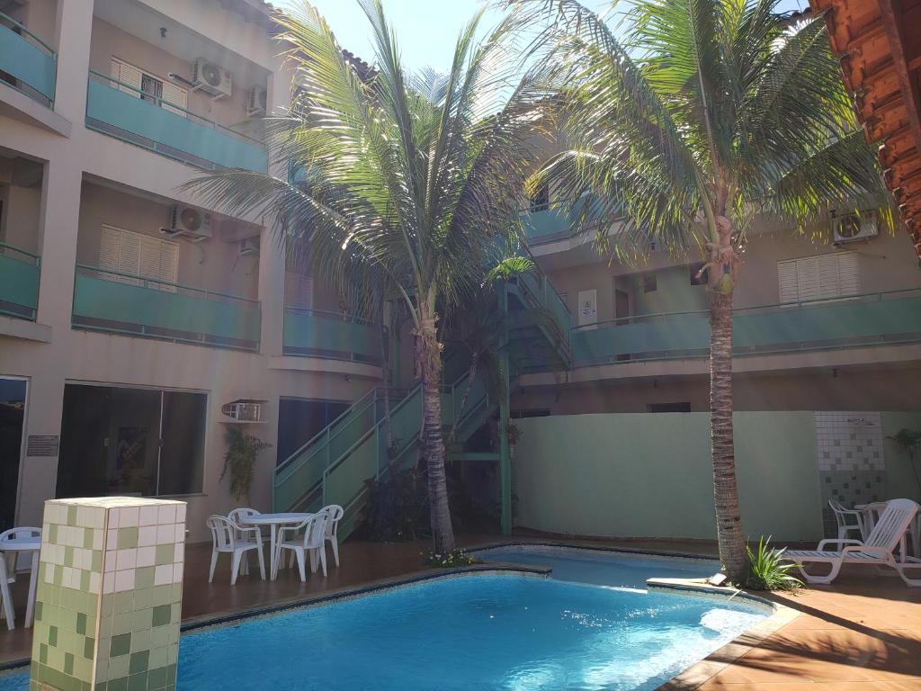 Sacadas do hotel com vista para piscina azul e duas palmeiras com algumas mesas e cadeiras brancas em volta durante o dia, ilustrando post Hotéis em Barretos.