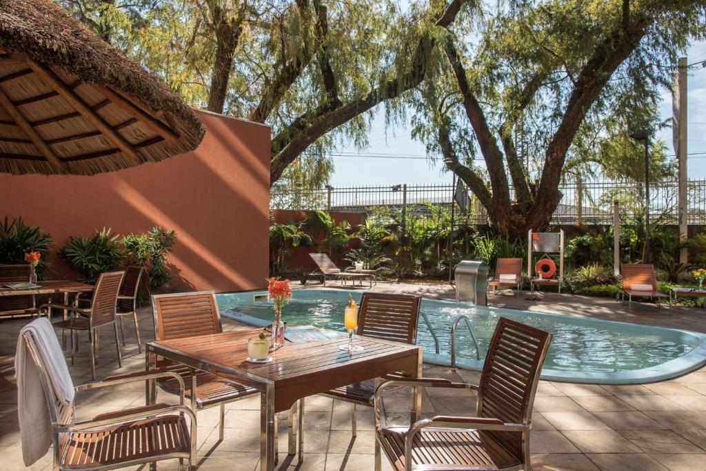Uma mesa com quatro cadeiras na frente e atrás a piscina com a cascata ligada. Para ilustrar post sobre Hotéis perto do Consulado Americano em Porto Alegre.