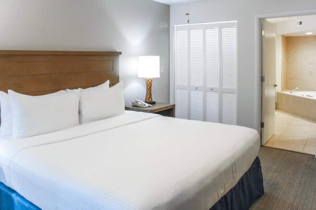quarto com guarda-roupa branco e cama de casal com mesinha  de madeira e luminária de ambos os lados do Polynesian Isles Resort, um dos hotéis em Kissimmee