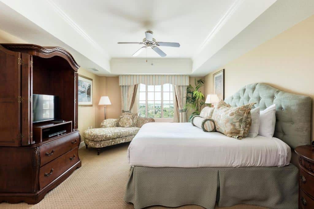 quarto do Reunion Resort & Golf Club, um resort em Kissimmee com cama de casal alta, móveis de madeira clássicos, com cortinas decoradas, ventilador de teto, sofá com detalhes de flores
