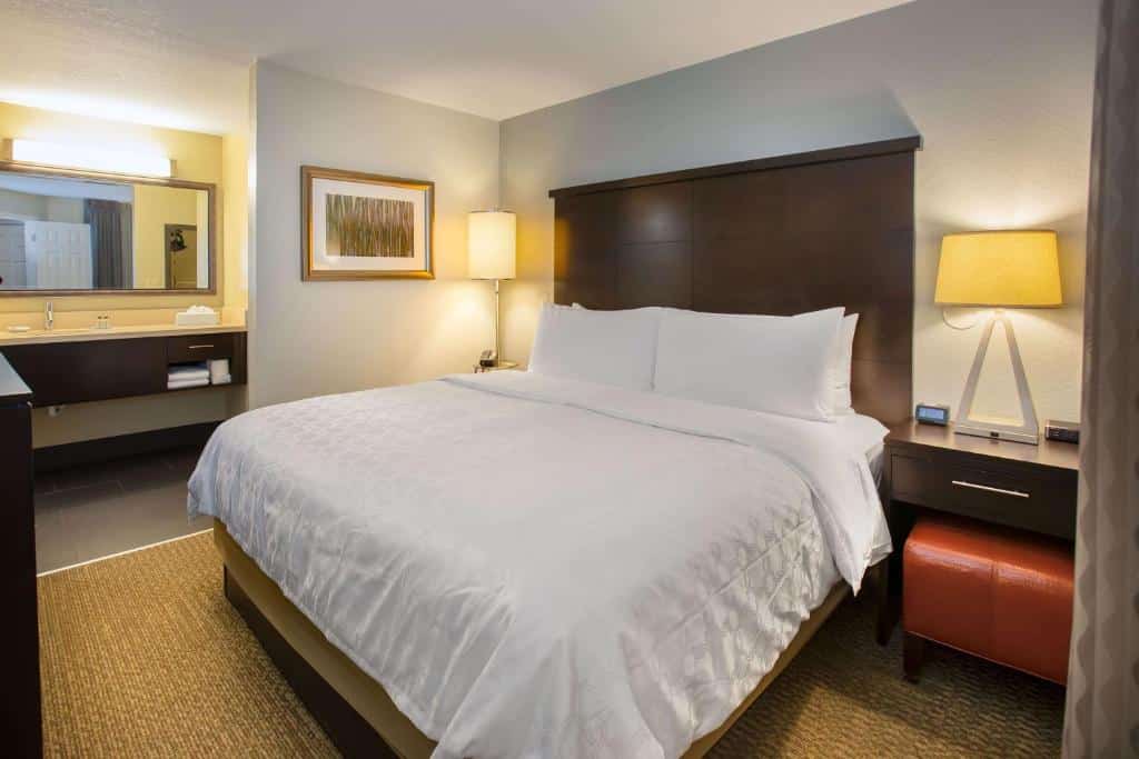 quarto com cama de casal com mesinha e luminária de ambos os lados e uma entrada grande para o banheiro no Sonesta ES Suites Orlando - Lake Buena Vista