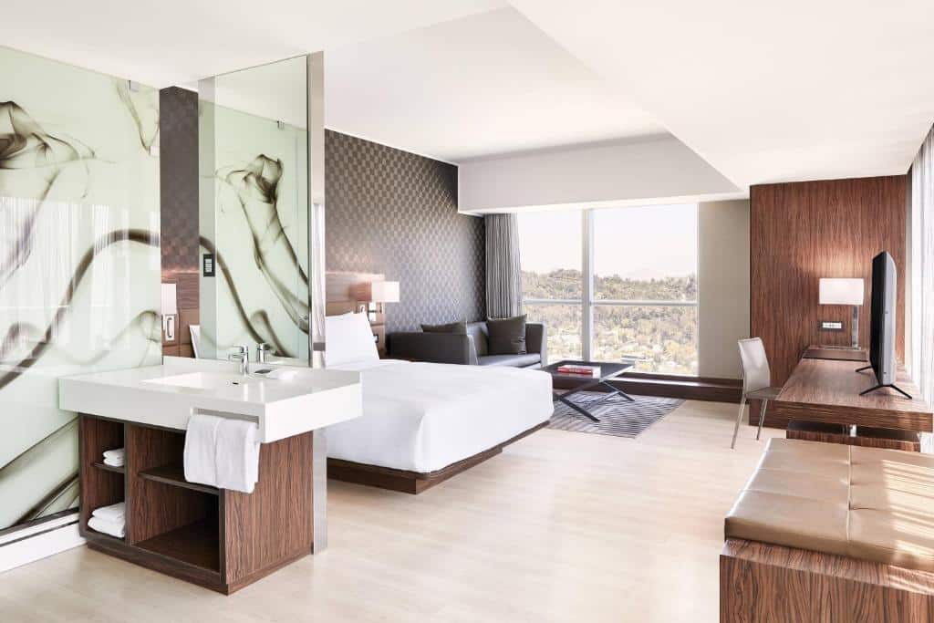 Quarto do AC Hotel by Marriott Santiago Costanera Center com pia a frente e ao fundo cama de casal, uma poltrona do lado esquerdo do quarto e uma mesa de trabalho com cadeira em frente a cama.