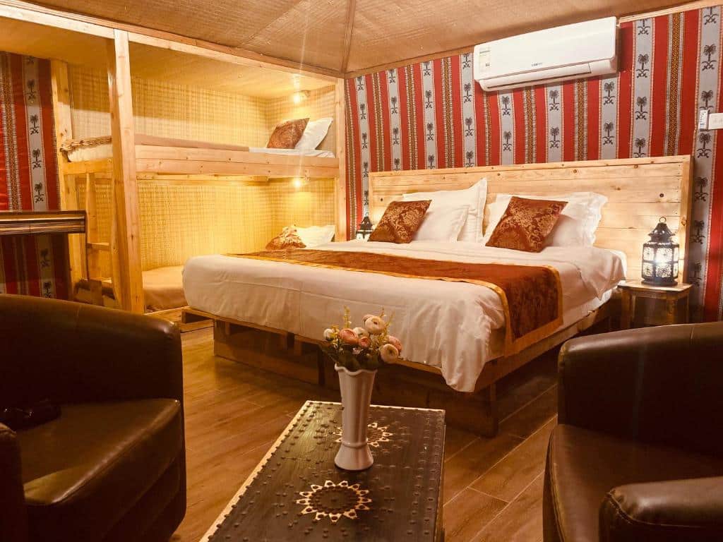 Quarto do Bedouin Oasis Desert Camp- Ras Al Khaimah com uma cama de casal, uma beliche, duas poltronas, um ar-condicionado de teto e uma mesinha de centro com uma vasinho de flor