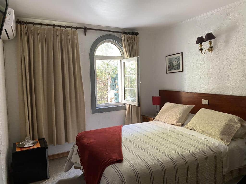 Quarto do Chilhotel com cama de casal no centro do quarto, do lado esquerdo da cama uma cômoda de madeira com luminária e em frente um frigobar.