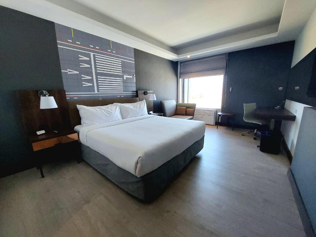Quarto do Courtyard by Marriott Santiago Airport com cama de casal no centro, duas cômodas de madeira do lado direito,do lado esquerdo do quarto uma poltrona e em frente a cama uma TV presa na parede.