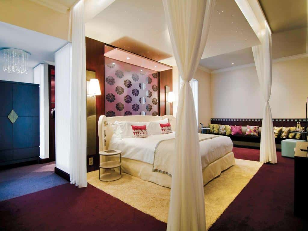 Quarto do Sofitel Legend The Grand, um dos hotéis de luxo em Amsterdam, com cama de casal, cortina em volta da cama e carpete vinho no chão.
