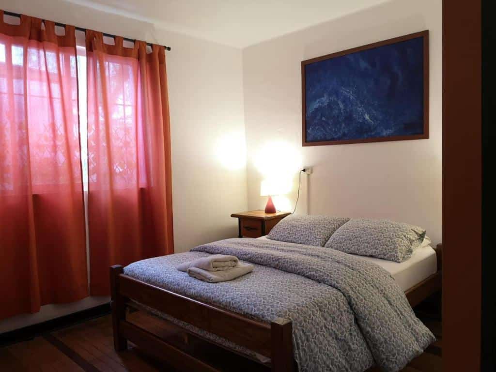 Quarto do  Hostal Vitalia com cama de casal do lado direito e do lado esquerdo uma cômoda ao lado da cama com luminária.