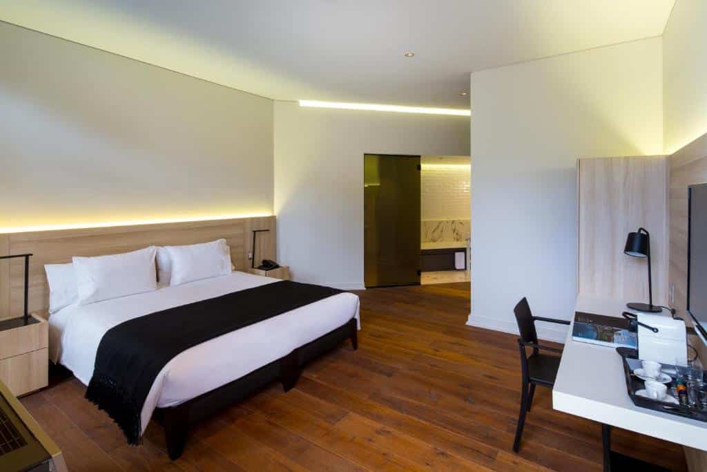Quarto do Hotel Altiplanico Bellas Artes com cama de casal do lado esquerdo do quarto e duas cômodas ao lado da cama e em frente a cama mesa de trabalho com cadeira.