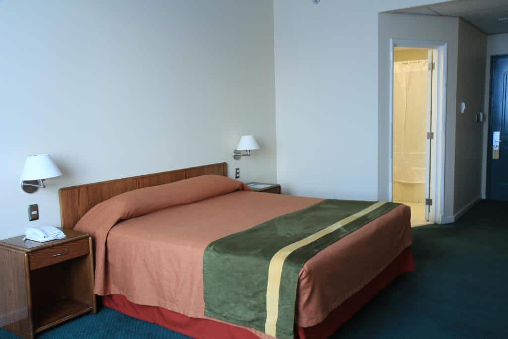 Quarto do Hotel Diego de Almagro Aeropuerto com cama de casal no centro do quarto com duas cômodas com luminárias ao lado da cama.