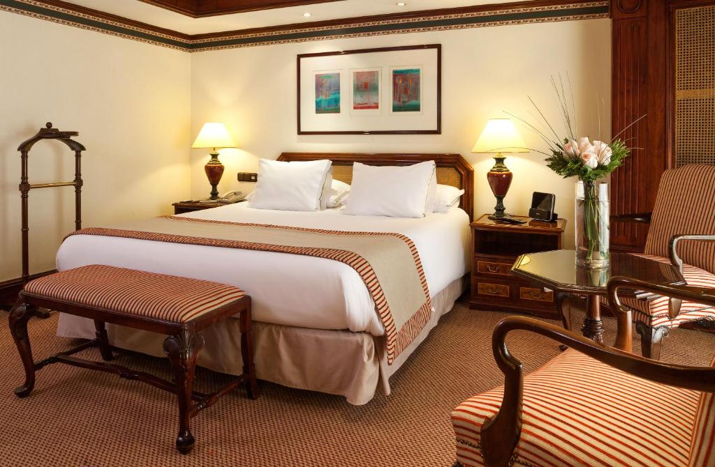 Quarto do Hotel Plaza San Francisco com cama de casal no centro do quarto, uma poltrona no pé da cama e uma poltrona do lado direito.