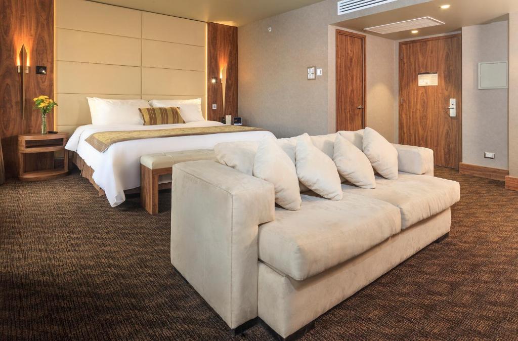 Quarto do Hotel Regal Pacific Santiago com cama de casal do lado esquerdo com duas cômodas ao lado e nos pés da cama um sofá com três lugares.