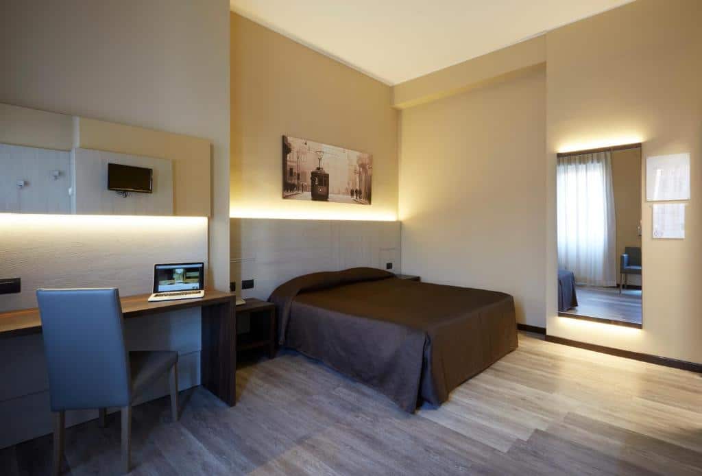 Quarto do Hotel Ritter com uma cama de casal,  um espelho, uma mesa de escritório com uma cadeira, o ambiente é espaçoso, para representar hotéis baratos em Milão