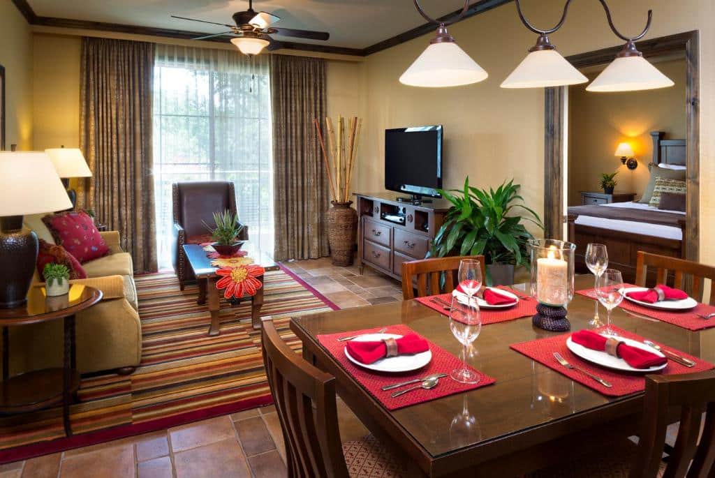 Sala de estar e jantar do Hyatt Residence Club San Antonio, Wild Oak Ranch com uma mesa com quatro lugares, um sofá e uma poltrona, há uma janela ampla do espaço com cortinas e um ventilador de teto, a decoração é em tons de marrom, vermelho e laranja