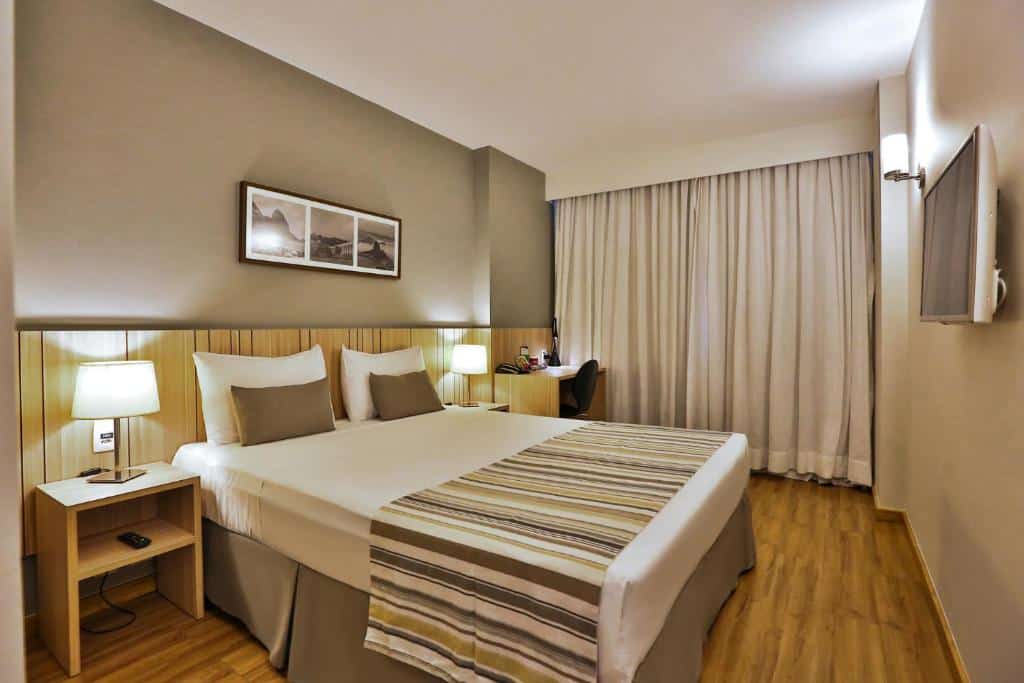 Uma cômoda nos dois lados da cama, uma cama no canto esquerdo e uma televisão no canto direito. Foto para ilustrar post sobre hotéis perto do Consulado Americano no Rio de Janeiro.