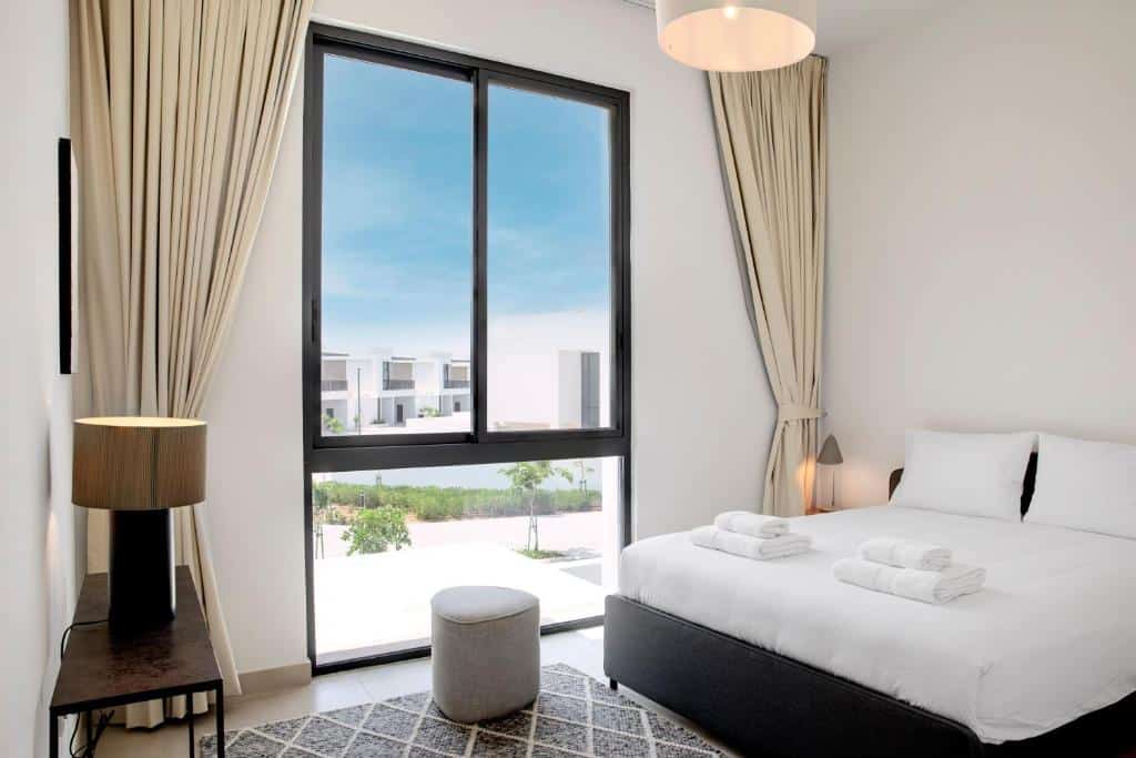 Quarto do Olala Oasis Homes com uma cama de casal, uma janela ampla com cortinas, um tapete cinza e uma mesinha com um abajur