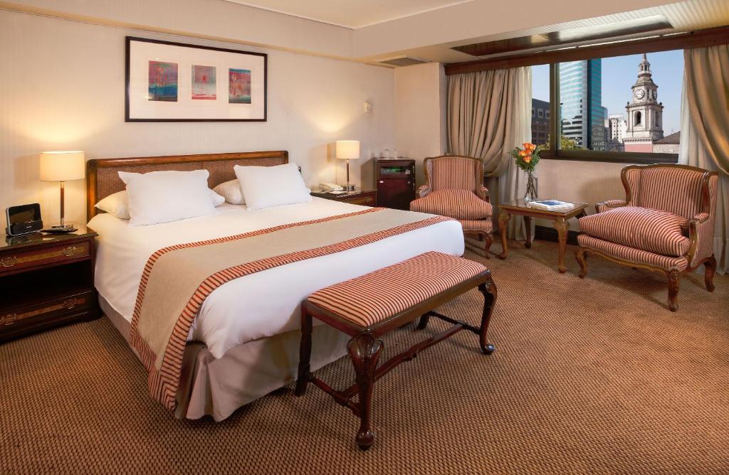 Quarto do Hotel Plaza San Francisco  com cama de casal ao centro do quarto, duas cômodas ao lado da cama com luminária e do lado esquerdo do quarto duas cômodas.