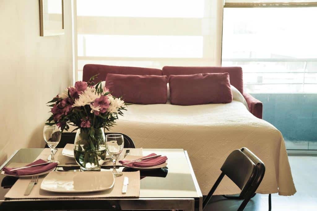 Quarto do Rentasuite Lyon com sofá cama a frente vinho e em frente a cama uma mesa com duas cadeiras com jogo de jantar em cima.