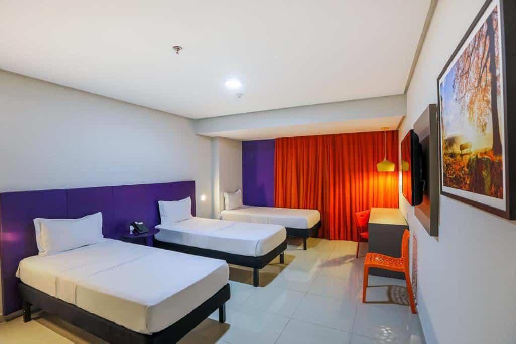 Quarto com três camas, mesa com cadeira, uma televisão e um quadro pendurado ao seu lado. Foto para ilustrar post de hotéis em Belém do Pará.