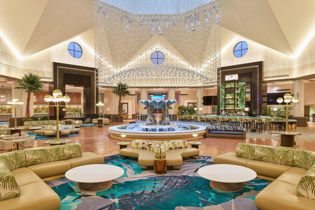 salão central com uma fonte grande decorada com peixes, mesas e poltronas e sofás em tons de dourado e azul, há um lustre que imita uma cascata acima no Walt Disney World Dolphin