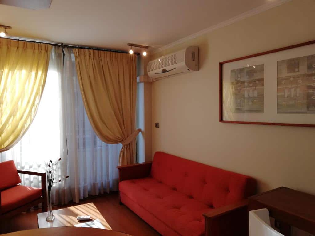 Sala do Andes Suites com sofá vermelho do lado direito uma mesa de centro e do lado esquerdo uma poltrona vermelha. Representa Airbnb em Santiago.