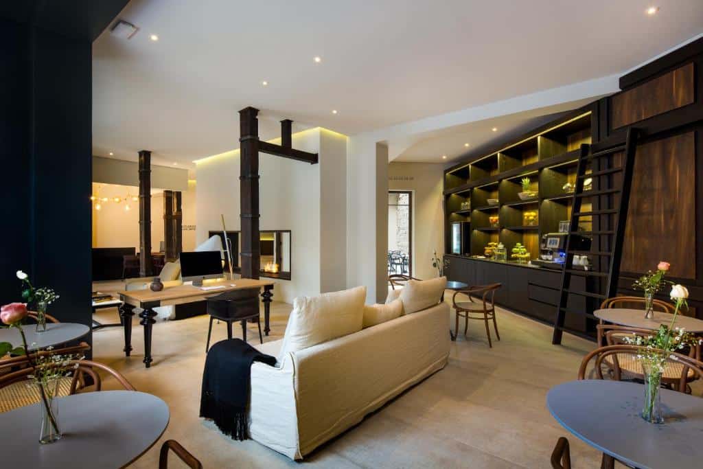 Sala de estar do Hotel Altiplanico Bellas Artes com sofás no ambiente, mesas e estante de madeira do lado esquerdo da imagem. Representa hotéis bem localizados em Santiago.