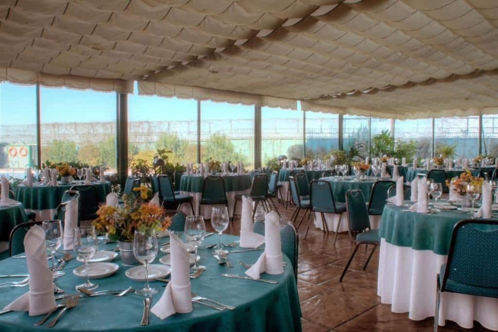 Sala de refeição do Hotel Diego de Almagro Aeropuerto com várias mesas com toalhas brancas, com pratos e taças em cima e cadeiras estofadas de azul claro. Representa hotéis perto do aeroporto de Santiago.