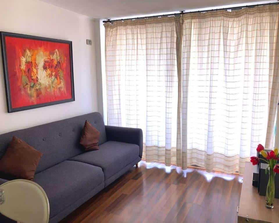 Sala do Departamentos Apartviews Cordillera com sofá azul claro do lado esquerdo uma cômoda em frente ao sofá. Representa Airbnb em Santiago.
