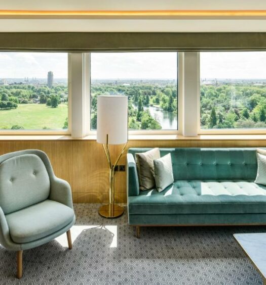 Sala de estar de uma das acomodações do Royal Lancaster London com um sofá com dois lugares, uma poltrona e uma janela ampla com vista para um parque, para representar hotéis em Londres para brasileiros
