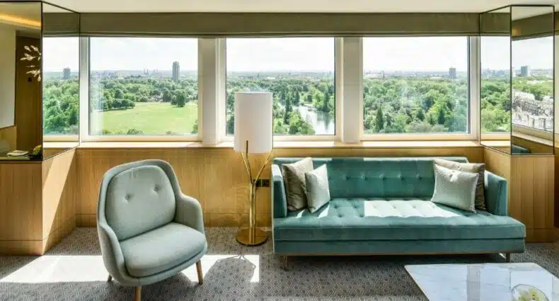 Sala de estar de uma das acomodações do Royal Lancaster London com um sofá com dois lugares, uma poltrona e uma janela ampla com vista para um parque, para representar hotéis em Londres para brasileiros
