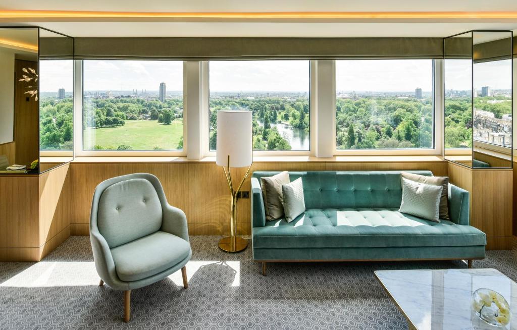 Sala de estar de uma das acomodações do Royal Lancaster London com um sofá com dois lugares, uma poltrona e uma janela ampla com vista para um parque, para representar hotéis em Londres para brasileiros