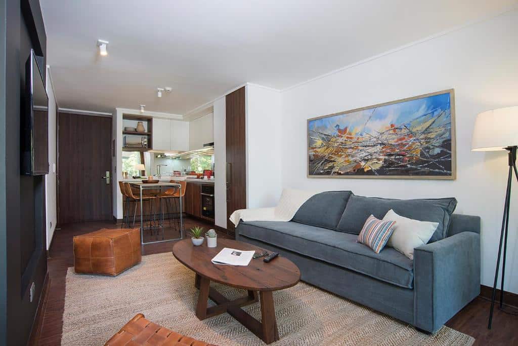 Sala de estar do The Place com sofá cinza claro, mesa de centro redonda de madeira e em frente uma TV. Representa aluguel de temporada em Santiago.