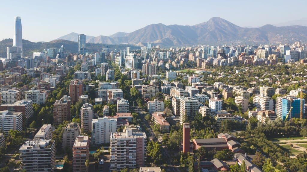 Vista da cidade de Santiago durante o dia com vários prédios em frente e ao fundo as montanhas.
