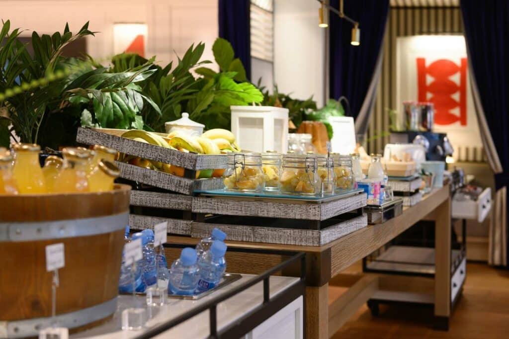 Café da manhã do Seventy Barcelona. Há diversas opções dispostas na mesa. Baldes com garrafas d'água e de suco de laranja, frutas, cereais e iogurte, entre outras coisas.