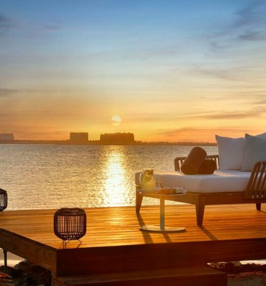 Um deck com uma espreguiçadeira virada para o mar de frente para o pôr do sol no The Ritz-Carlton Ras Al Khaimah, Al Hamra Beach