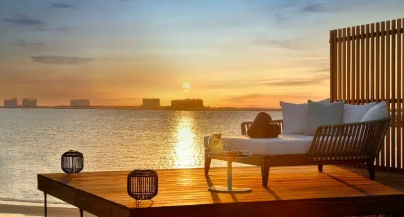 Um deck com uma espreguiçadeira virada para o mar de frente para o pôr do sol no The Ritz-Carlton Ras Al Khaimah, Al Hamra Beach, para representar resorts em Ras Al Khaimah