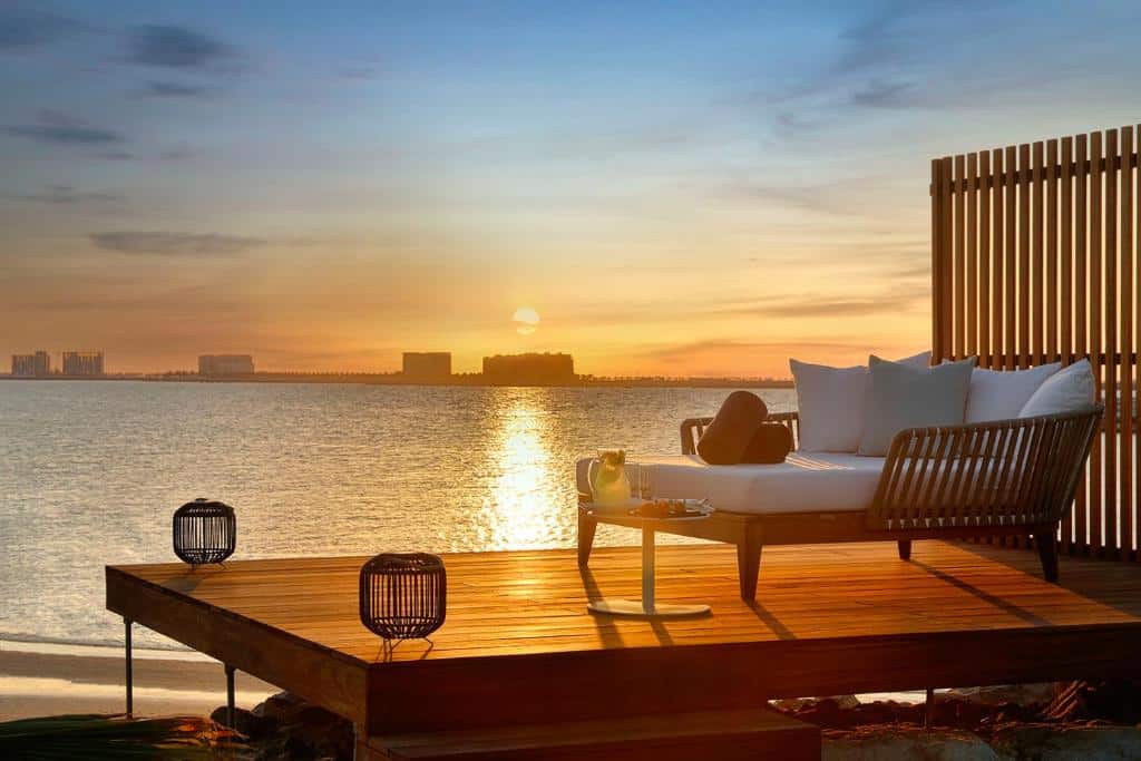 Um deck com uma espreguiçadeira virada para o mar de frente para o pôr do sol no The Ritz-Carlton Ras Al Khaimah, Al Hamra Beach