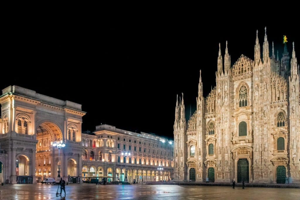 Uma ampla praça de frente para a catedral de Milão, uma construção antiga em estilo gótico com diversas torres