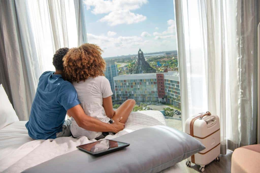 casal de pessoas negras abraçado sentado na cama com vista direta para o Volcano Bay no Universal's Aventura Hotel, um dos hotéis da Universal em Orlando