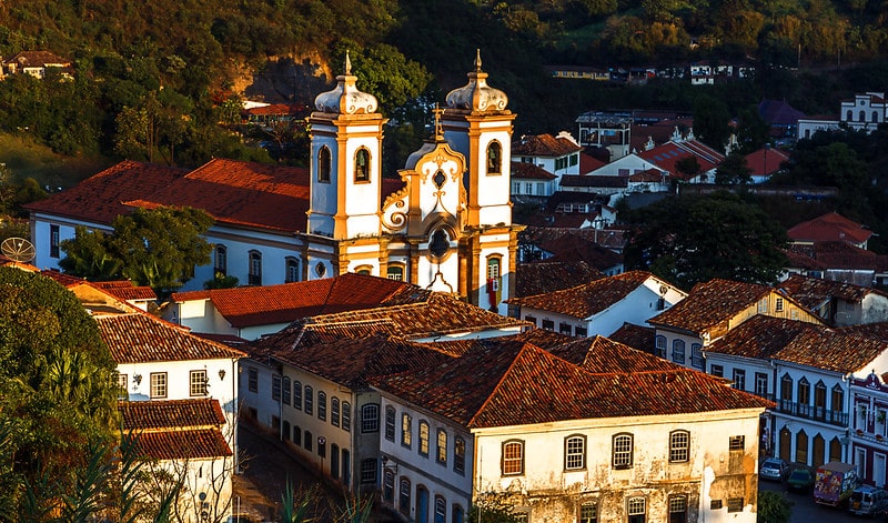 Cidade histórica de Ouro Preto. Vemos construções e prédios com arquitetura preservada da época colonial. Em destaque, há uma igreja que chama atenção no centro.