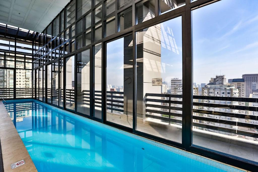 Piscina interna do hotel Radisson Blu. As janelas tem bordas pretas e a piscina é longa, cobrindo uma longa área vertical. É possível ver a vista dos prédios de São Paulo.