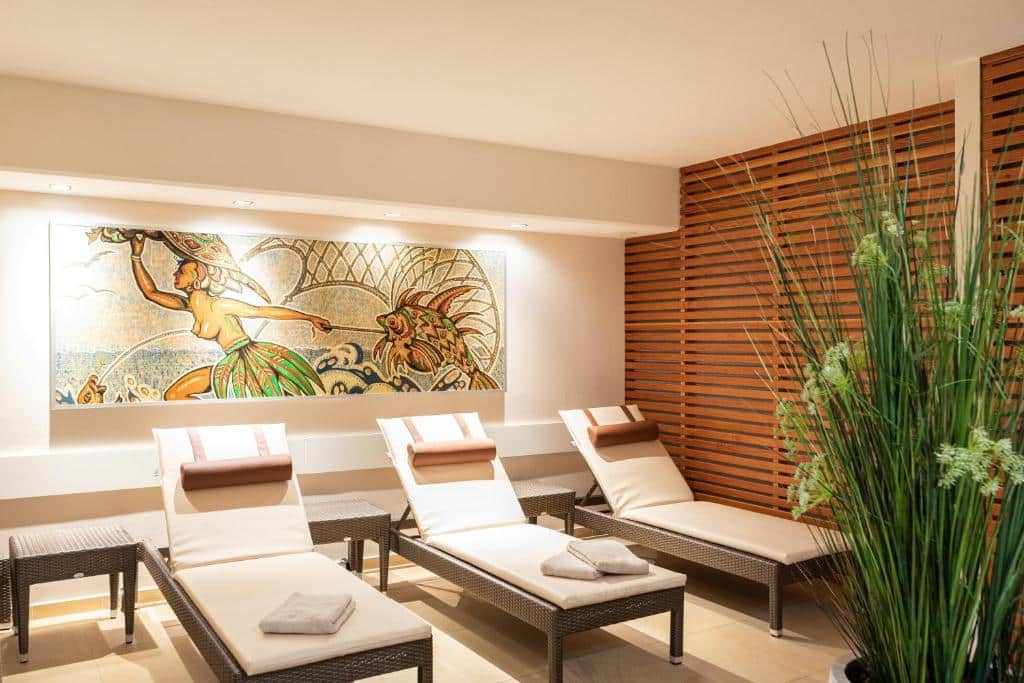 Área do spa do hotel, com três espreguiçadeiras brancas, quadro na parede, detalhes de madeira e uma planta verde, ilustrando post Hotéis em Salzburg.