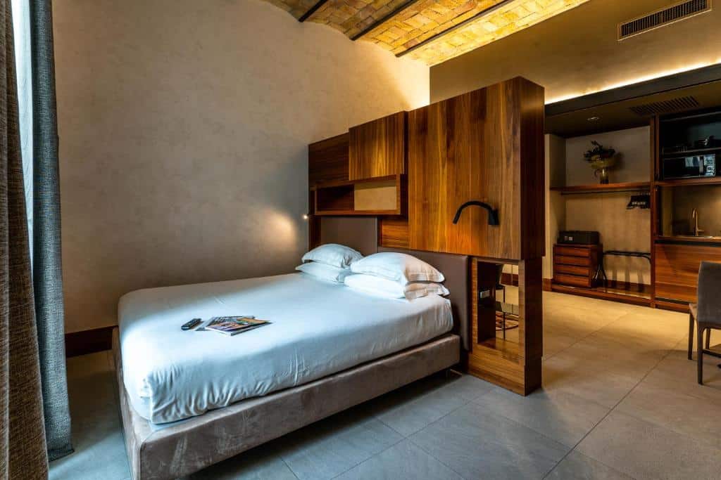 o Gasometer Urban Suites, um aluguel de temporada em Roma, com cama de casal com uma separação atrás que é um guarda-roupa moderno, e uma sala de estar ao fundo com móveis de madeira, há uma janela em frente à cama
