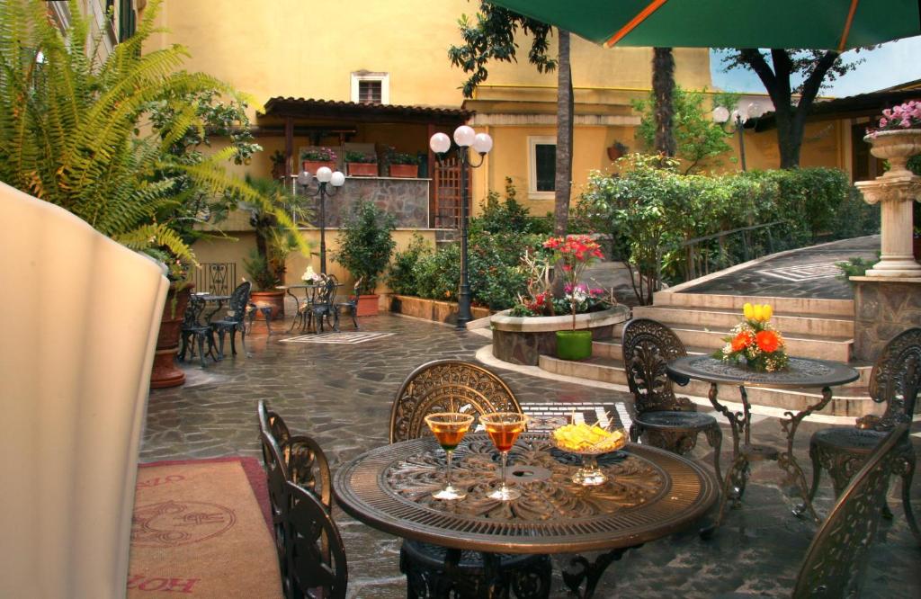 área comum do Hotel Villa San Lorenzo Maria, um dos hotéis baratos em Roma, com mesa e cadeiras de ferro vintage, uma praça grande com gazebos e plantas verdes por todo os arredores