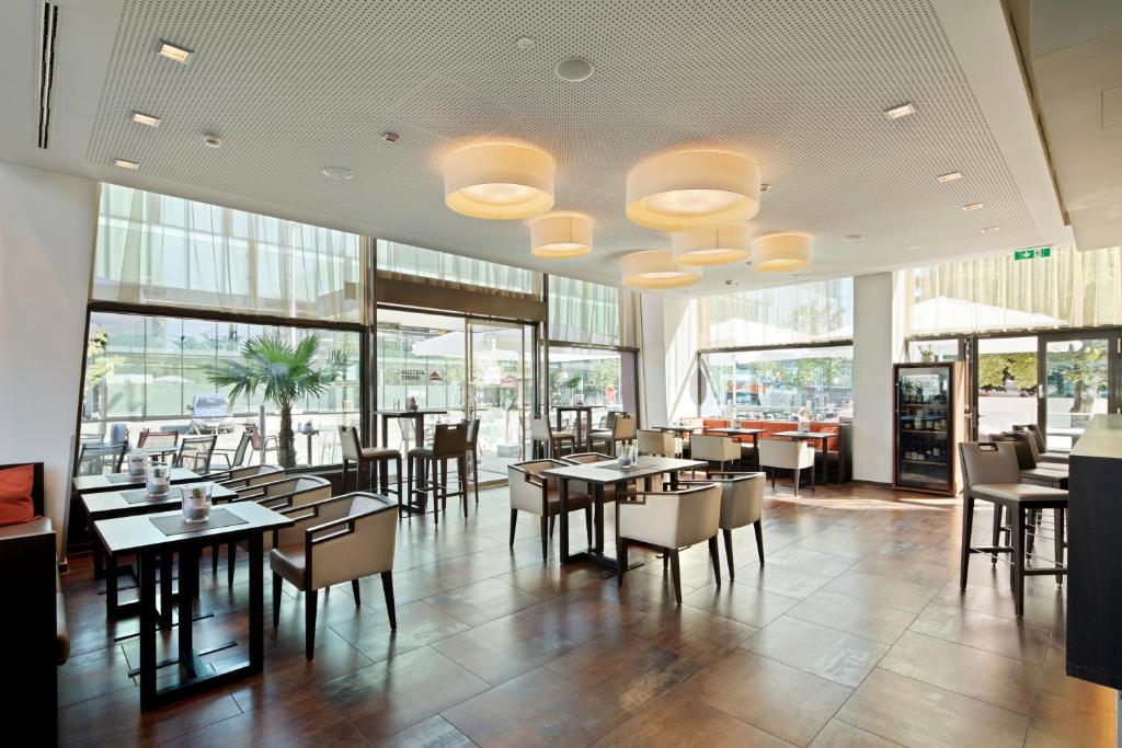 Parte do hotel para fazer as refeições com várias mesas e cadeiras em tons de marrom e branco, lustres redondos no teto e porta de vidro com vista para a rua, ilustrando post Hotéis em Salzburg.